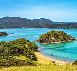 Malerische Bucht auf Neuseeland mit türkisblauem Wasser, kleinen Inseln und bewaldeten Hügeln im Hintergrund.
