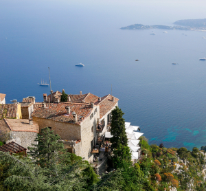 Blick von einer Anhöhe auf Häuser mit Terrakottadächern an der Côte d’Azur und das tiefblaue Mittelmeer.