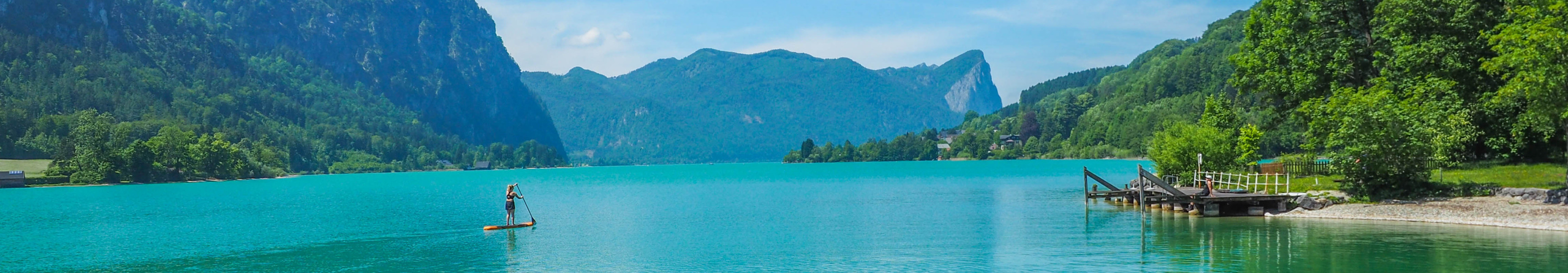 Panoramablick auf den türkisblauen Wolfgangsee in Österreich mit Bergen, Steg und Stand-up-Paddler