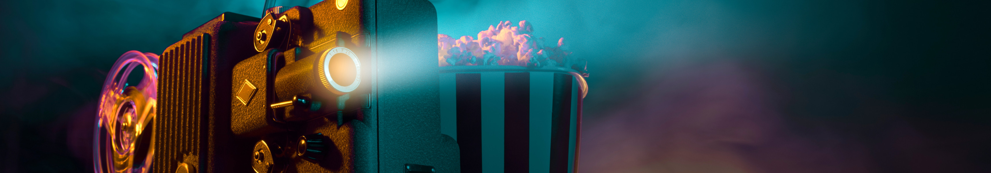 Alter Filmprojektor mit laufender Filmrolle, daneben eine gestreifte Popcorntüte, im Hintergrund bunte Licht- und Rauch­effekte.