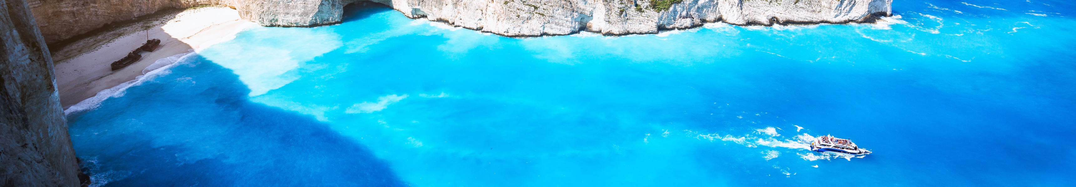Die berühmte Navagio-Bucht auf Zakynthos in Griechenland mit türkisblauem Wasser, weißen Klippen, einem Schiffswrack am Strand und einem Ausflugsboot im Meer.