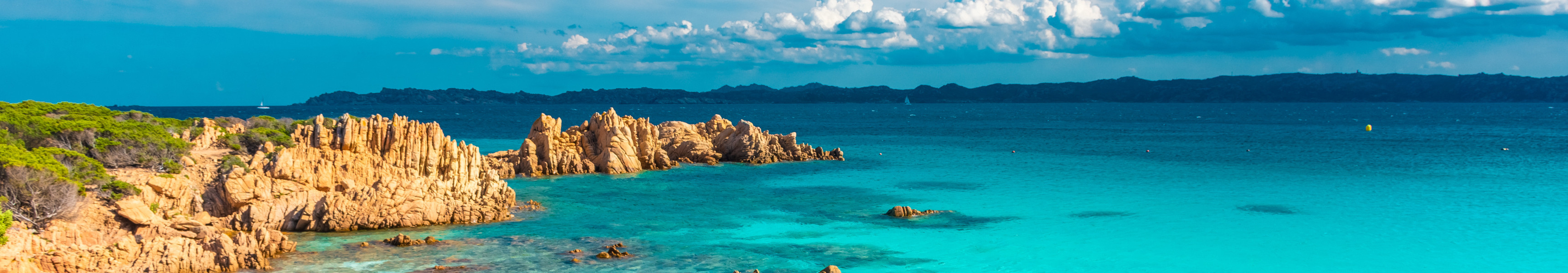 Traumstrand mit türkisblauem Wasser und rötlichen Felsen auf Sardinien.