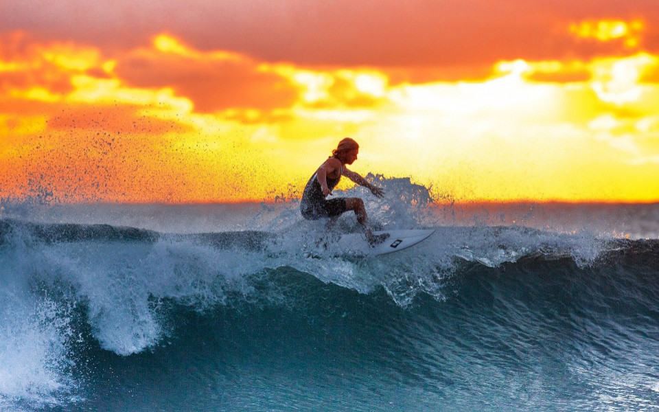 Mann surft auf einer Welle mit Sonnenuntergang