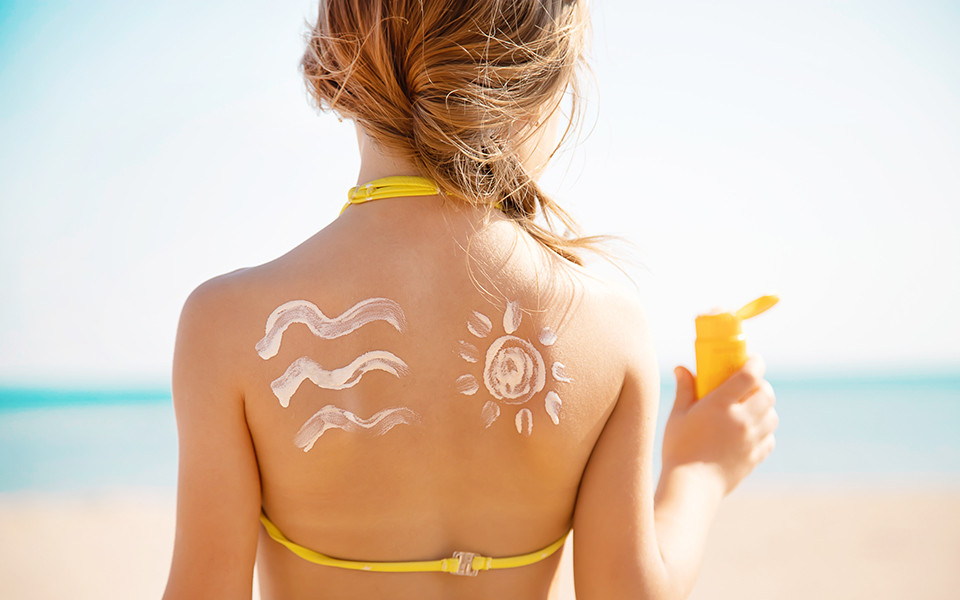 Rücken einer Frau mit Sonnencreme am Strand