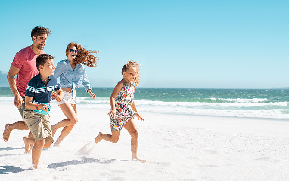 Familienurlaub Frühbucher: Familie läuft am Strand entlang im Familienurlaub