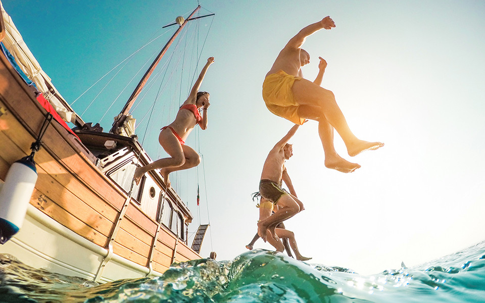Frühbucher Angebote: Freunde springen vom Boot aus ins Meer