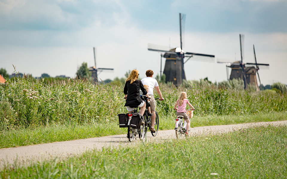 Familie fährt Rad zwischen Windmühlen und Wiese