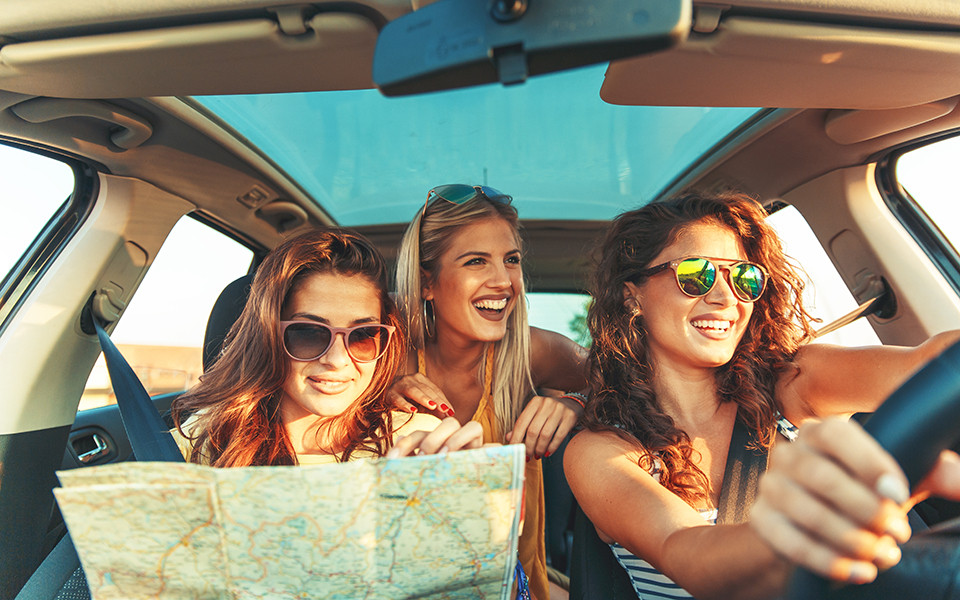 Drei Frauen im Auto mit Stadtplan auf dem Weg zu einem Kurzurlaub