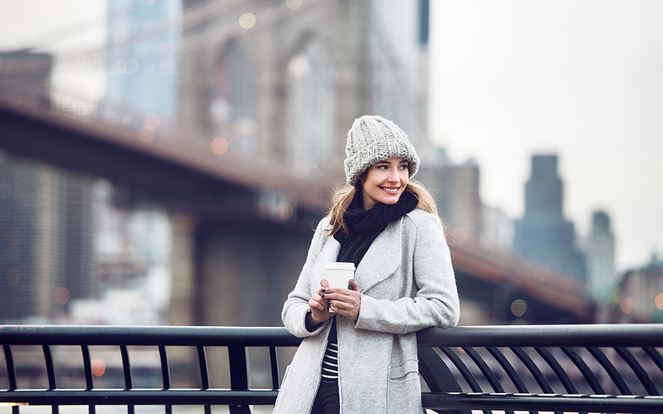 Frau mit Winterkleidung auf Brücke mit Kaffee