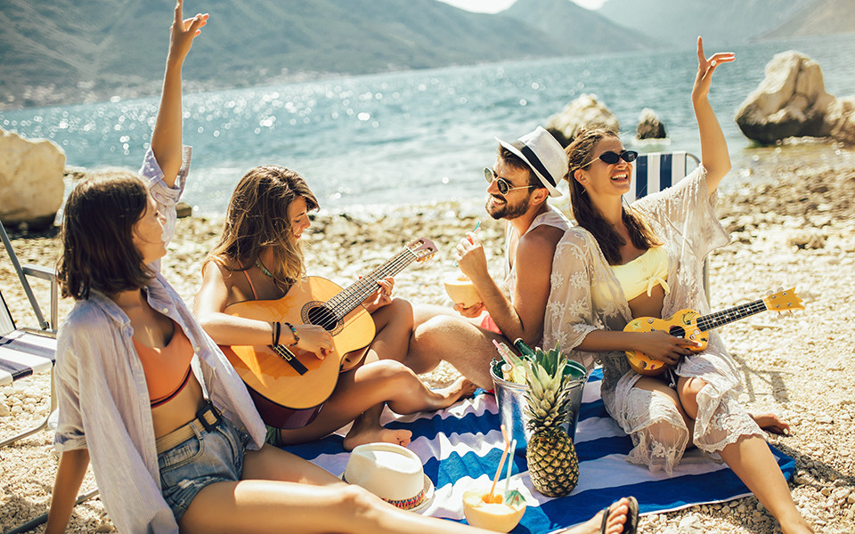 Super Last Minute Urlaub: Freunde am Strand spielen Gitarre 