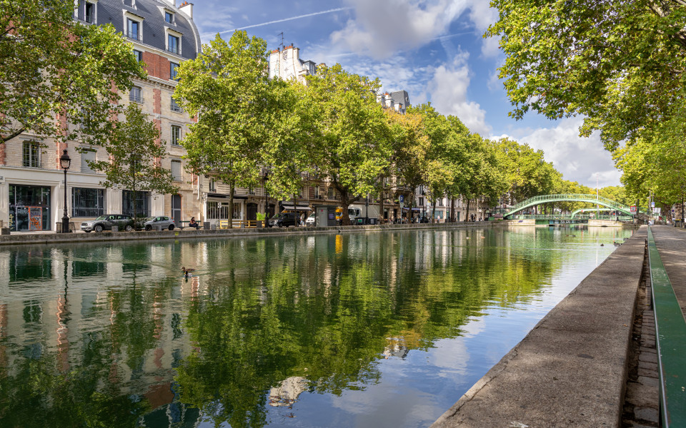 Idyllischer Canal Saint-Martin in Paris mit grünen Bäumen, Brücke und spiegelndem Wasser