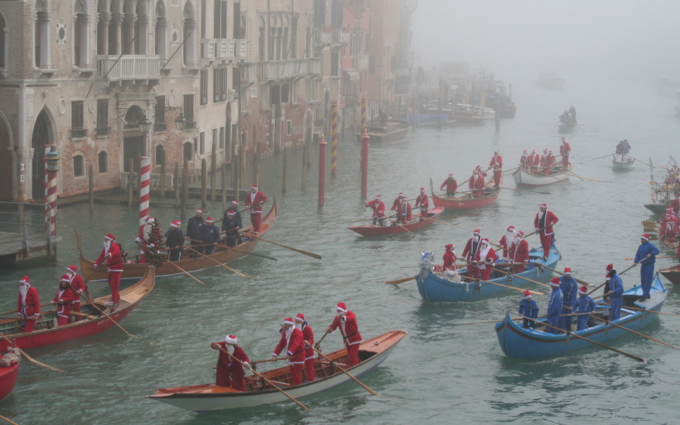 Gondeln voller als Nikolaus verkleideter Ruderer auf dem Canal Grande in Venedig bei winterlichem Nebel – traditionelle Nikolausfahrt in Italien.